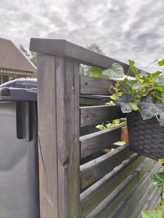 Staketstolpe i trä kapat snett vid toppen intill en hängande blomkorg och plank.