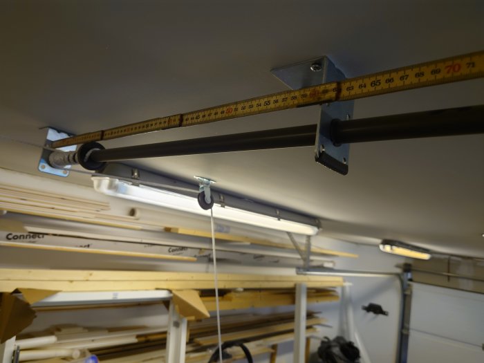 Mätband visar cc-mått på hängskenor i ett garage, med virke staplat i bakgrunden.