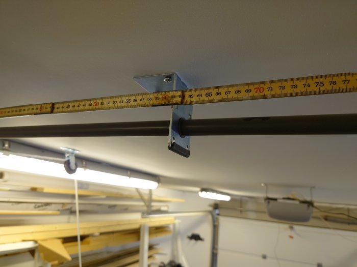 Måttband visar avstånd mellan monteringspunkter på hängande räls i en verkstad.
