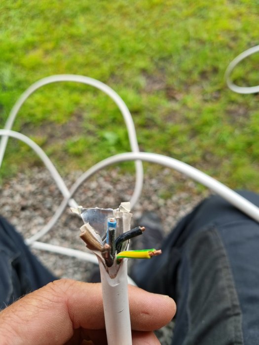 Person håller skärmad kabel med avskalade ändar utomhus, okänd kabeltyp utan biledare.