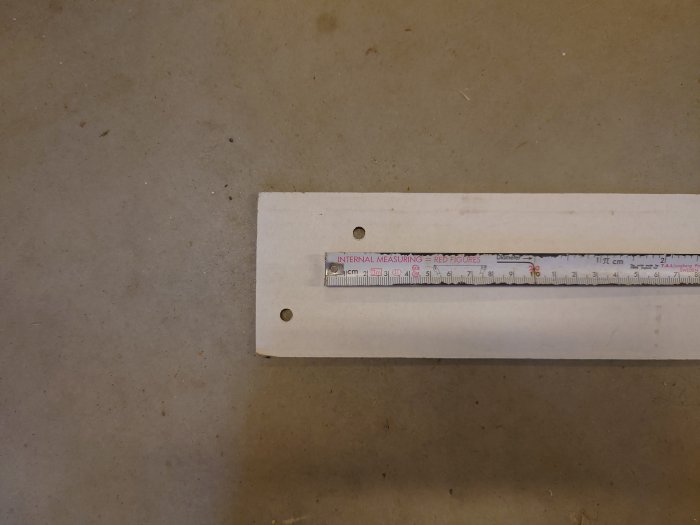 Monteringsmall med märkta hål och mätsticka ovanpå som visar CC90 avstånd på en betongyta.