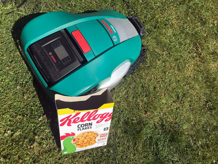 Bosch Indego robotgräsklippare på en Kellogg's Corn Flakes kartong på gräsmatta.