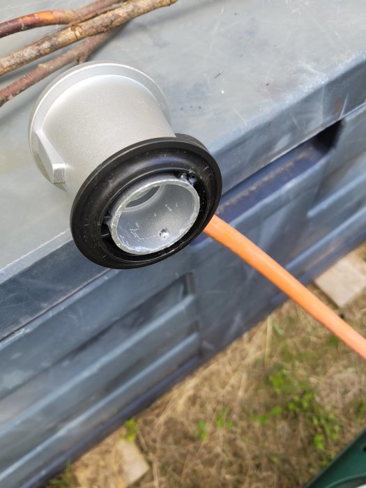 Närbild av en ogasluten anslutning till en maskin med en synlig orange slang och en öppen koppling.