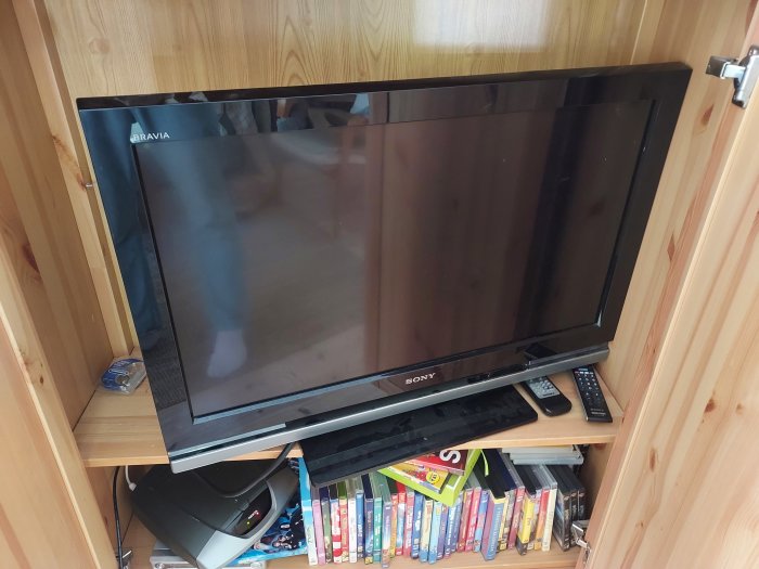 Äldre Sony Bravia-TV, digitalbox och DVD-filmer i en trähylla, användare har problem med TV-signalen.