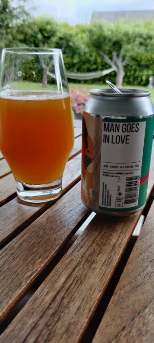 Halvfylld ölglas bredvid mangoölburk från Nyköping Brewing på träbord utomhus.