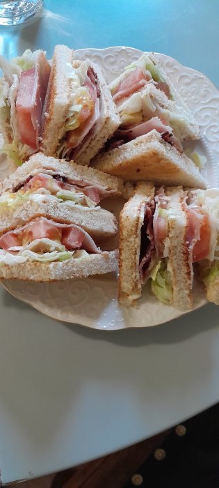 Club sandwich med skinka, ost och sallad på vitt tallrik.