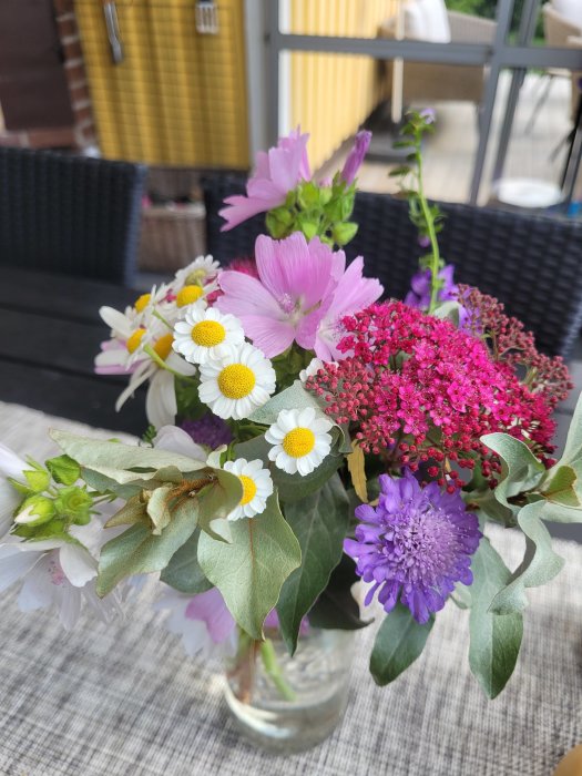 Färgglad bukett med blandade trädgårdsblommor i en klar glasvas på ett bord.