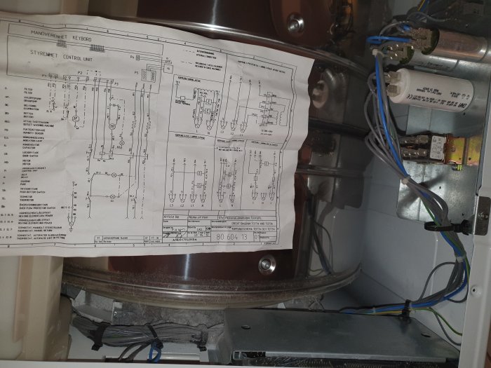Öppnad torktumlare med elschema och interna komponenter synliga.