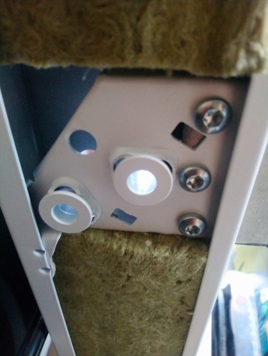 Närbild på en dörrkarm med karmhylsor och skruvar mot en bakgrund av isoleringsmaterial.