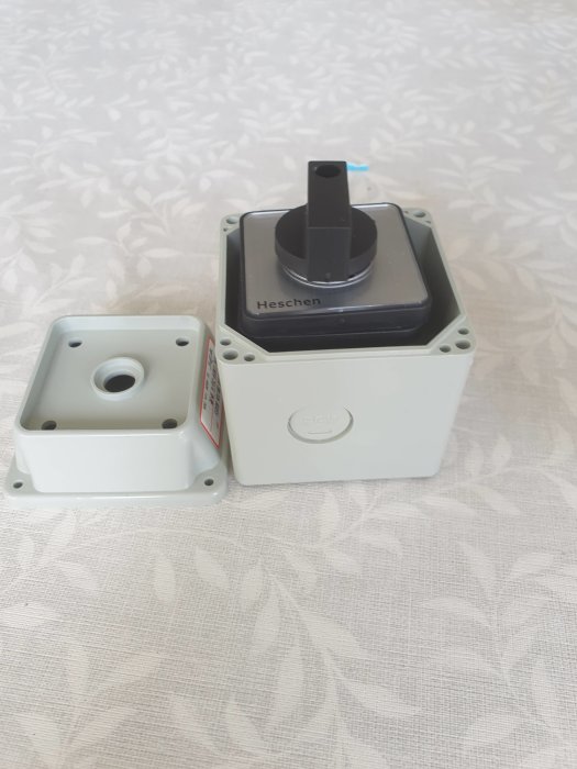 En liten elektrisk kopplingslåda och dess lock på ett mönstrat tygunderlag.