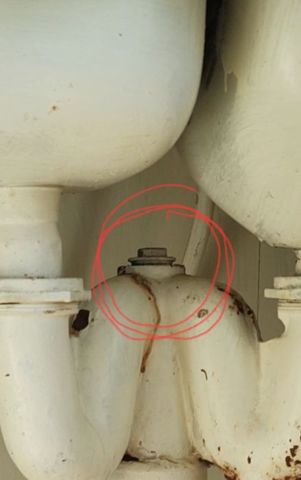 Mässingsstos för avlopp markerad med röd cirkel på vit avloppsrörinstallation.