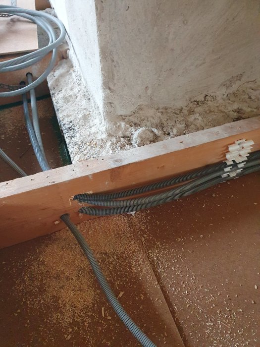 Borrhål i träregel med genomdragna kablar vid betongvägg och isolering.