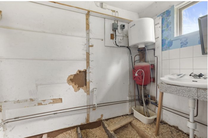 Renoveringsbehov i badrum med skadade väggar, vattenberedare och rörinstallationer.