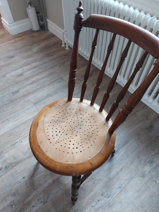 Träpinnstol med sliten skålad plywood-sits och spjälrygg står på laminatgolv.