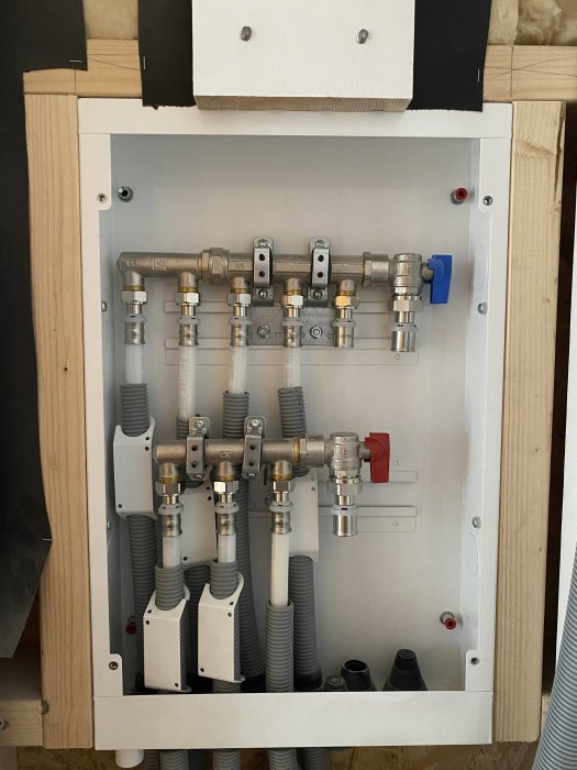 Installationsvy av en väggmonterad värmefördelare för golvvärme med rör och ventiler.