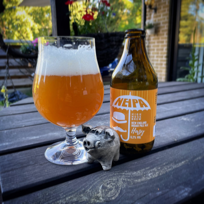 Ett glas öl och en flaska märkt NEIPA med en lergris på ett träbord.