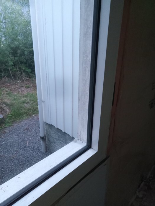 Stort fast aluminiumfönster från insidan, skruvar ej synliga, vid vägg och plåtfasad.