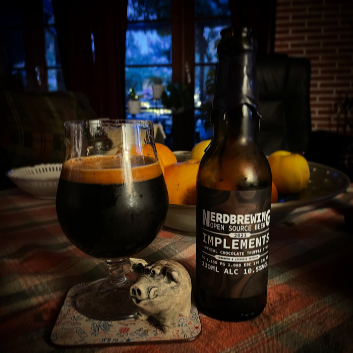 En mörk öl i ett glas bredvid en flaska märkt "Nerdbrewing", på ett bord med citroner i bakgrunden.