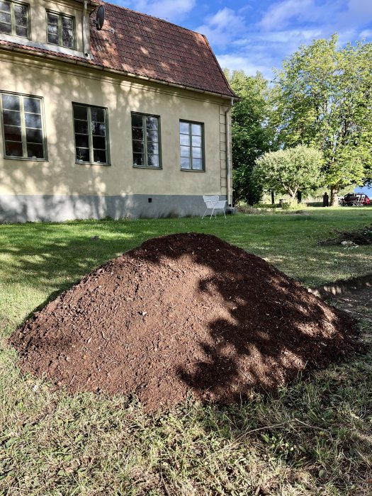 En hög med fin kompostjord bredvid ett hus på en gräsmatta, resultat av komposterad kastanj.