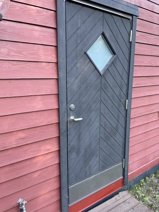 Dörr på gästhus med fräst in plåt i tröskeln och röd fjällpanelvägg.