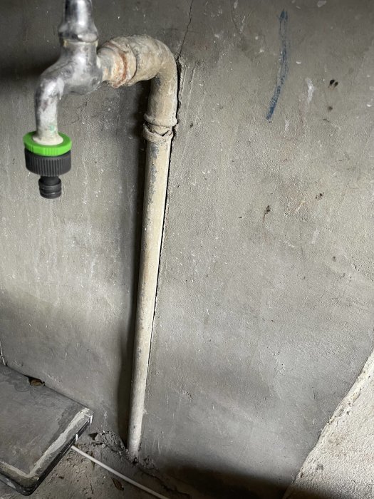 Gammal kran och rör i garaget, med 90-graders böj och rör ingjutet i vägg.