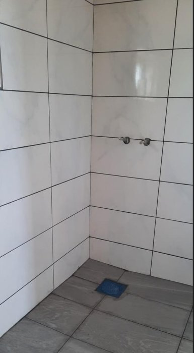 Hörn av badrum med kaklade väggar och grått klinkergolv. Framstickande PEX slangar väntar på installation.
