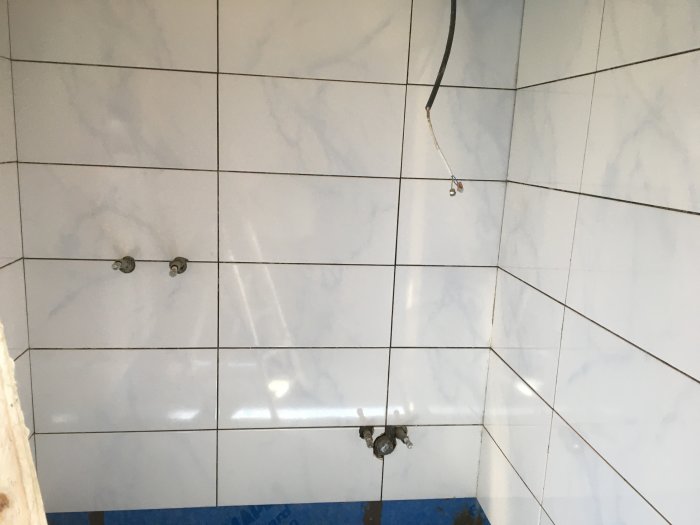 Vägg med kakel och utstickande VVS-installationer: pex-rör och avstängningsventiler.