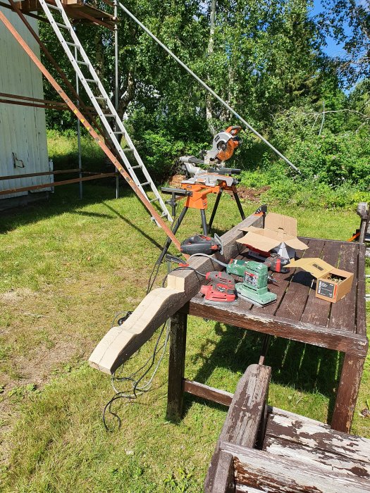 Utomhus arbetsplats med pågående tillverkning av taktass på ett träbord med verktyg och en stege i bakgrunden.