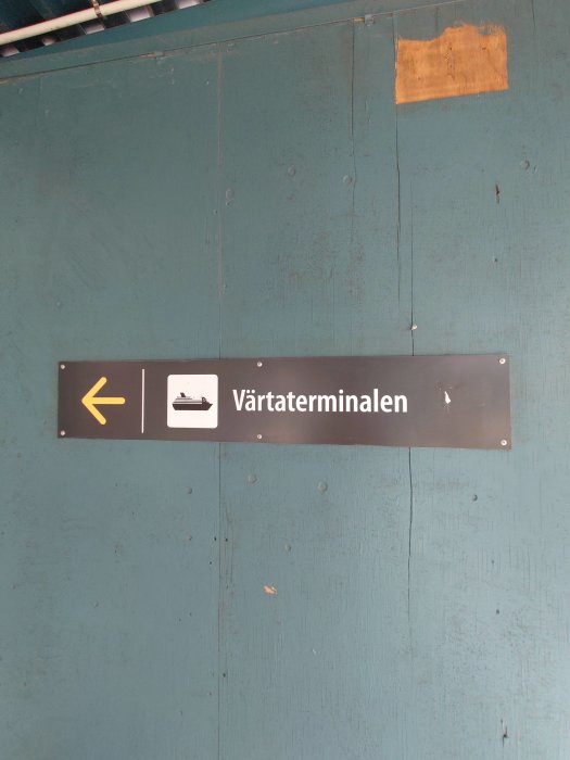 Skylt med pil och symbol för väntsal som pekar åt vänster, texten 'Värtaterminalen' mot en grön bakgrund.