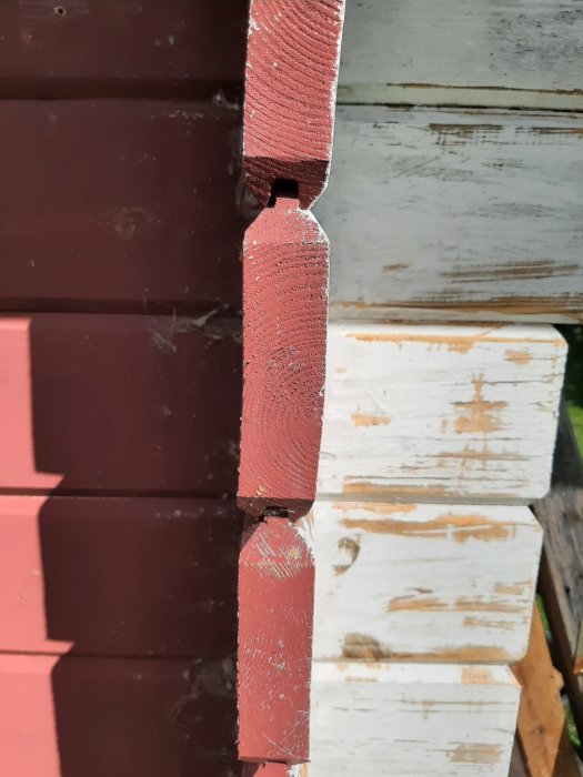 Närbild på skadade, färgade träplankor på ett förråd som behöver bytas ut.