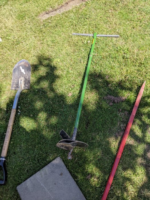 Spade, skurupsborr och markeringstång på gräsmatta, används för att borra i lerjord.