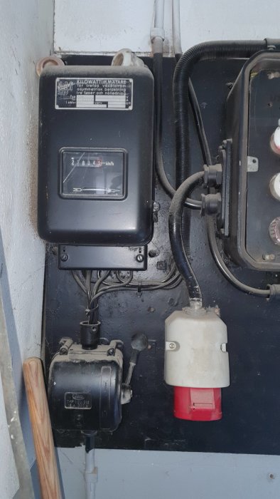 Elanläggning i garage med kilowattimräknare, strömbrytare och säkringar på en svart panel.