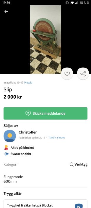 Äldre bänkslipmaskin med rostbrun slipsten och grön kropp på ett schackrutigt golv.