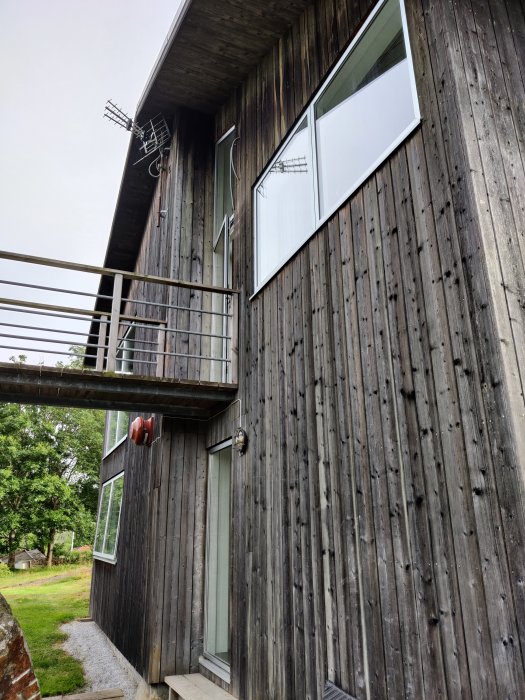 Fasaden på ett hus med väderbiten träpanel och galvade spikar som håller bra, med synliga fönster och balkong.