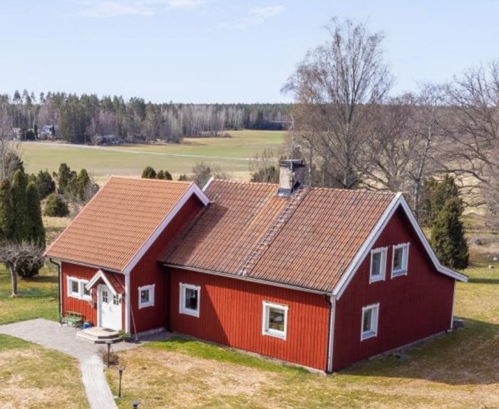 Röd villa med tegeltak och betongpannor bland landskap med synlig stege på taket.