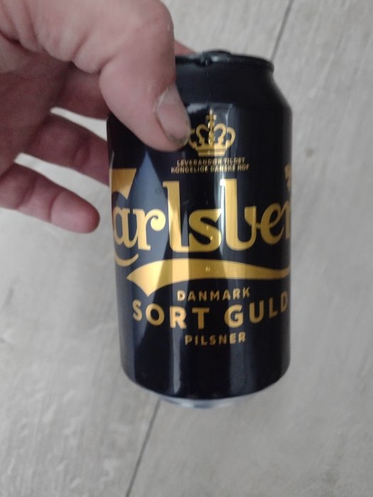 Hand håller en burk Carlsberg Sort Guld öl.