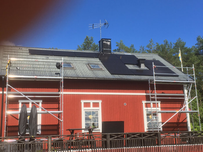 Rött hus med nästan färdiginstallerade solpaneler på taket, ställning vid sidan och en svensk flagga.