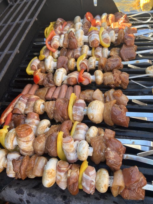 Grillspett med kött, champinjoner och färgrika paprikabitar på en grill.