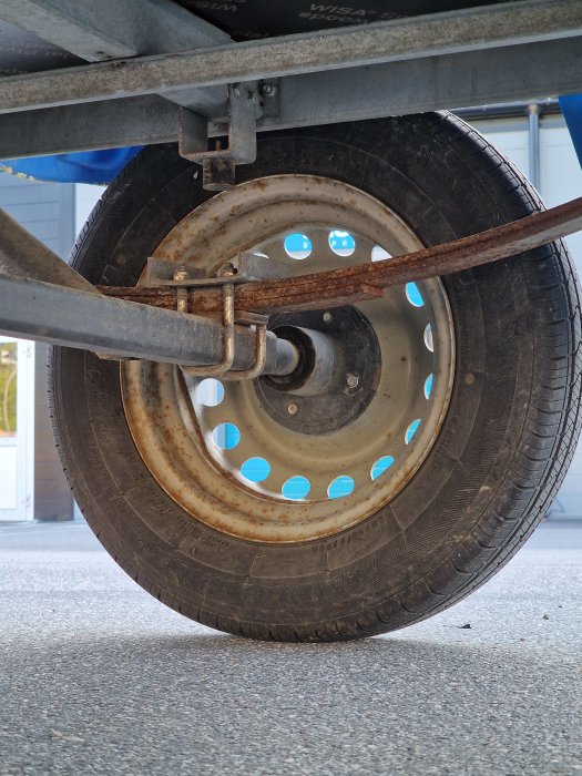 Närbild på släpvagnshjul med synlig rostig axel och hjulbultar, behov av underhåll.