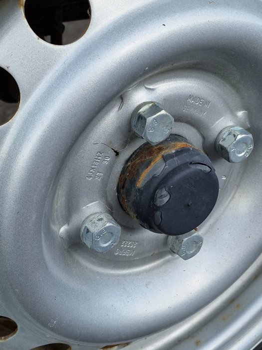 Närbild av ett bilhjul med fokus på navkapseln och hjulbultar, synliga tecken på slitage och rost.