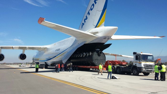 Lastbil som kör ut en stor cylinder från lastutrymmet på ett Antonov An-124 flygplan.