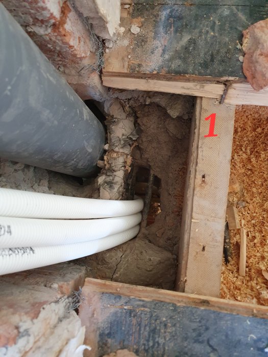 Bild på öppen golvkonstruktion med synliga avloppsrör, pexrör, och isolering inför renovering.