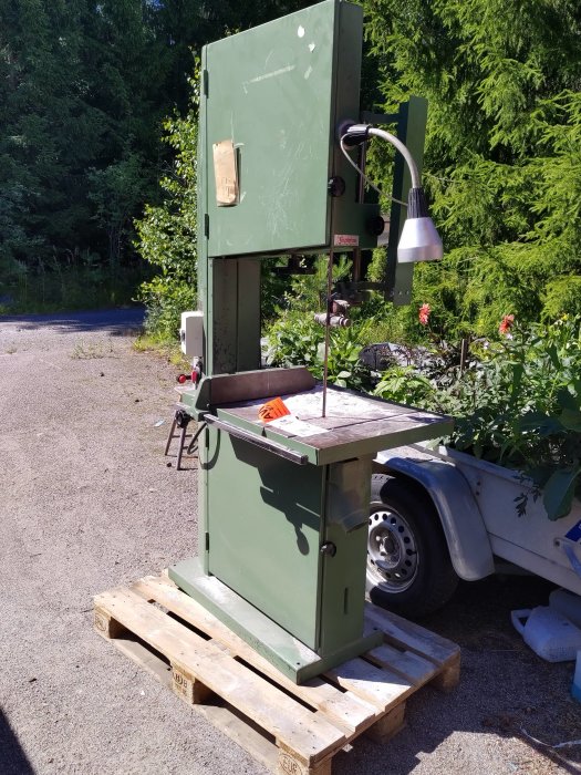 Meber SR 600 bandsåg placerad på en träpall utomhus, nära en skog och blommor, med en arbetslampa fäst ovanför.