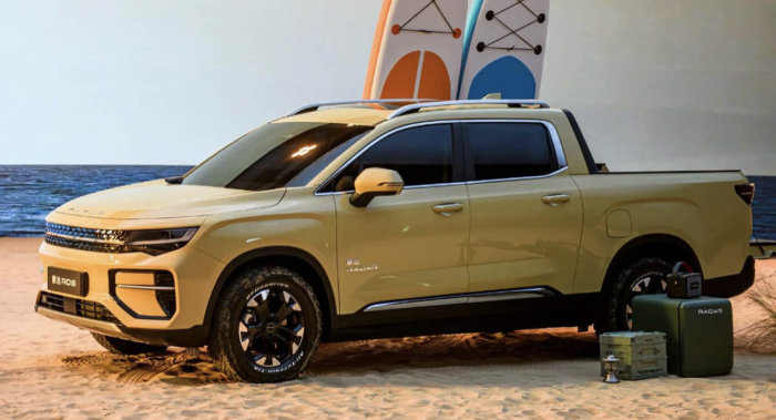 Gul eldriven pickup, Radar R6, parkerad på strand med surfbrädor i bakgrunden.