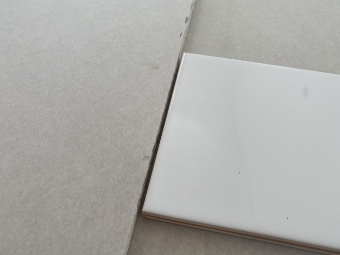 Närbild på kanten av en vit kakelplatta som möter en 13mm gipsskiva.