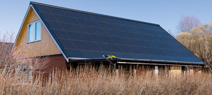 Hus med solcellspaneler på taket, plåtdetaljer nedtill och på sidorna, samt en svensk flagga.