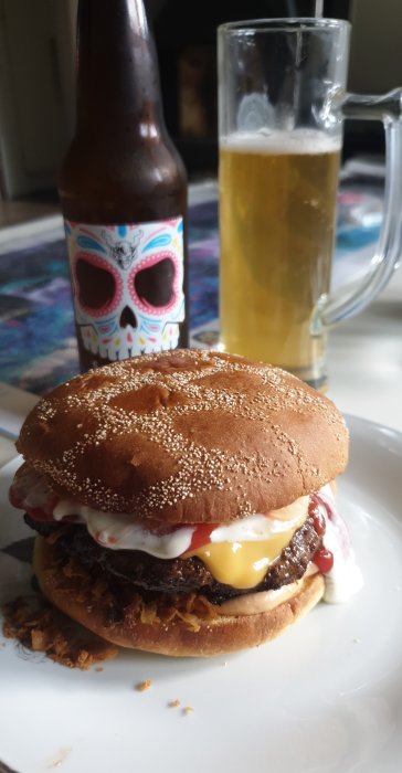 Juicy hamburger with toppings on a plate, a beer bottle and glass in the background.