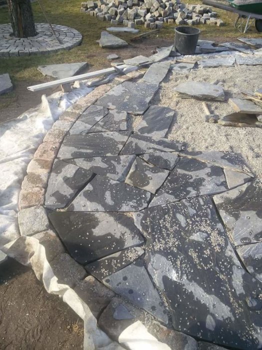 Skifferstenar som är ojämnt lagda för att skapa ett stenmönster på marken med byggmaterial i bakgrunden.