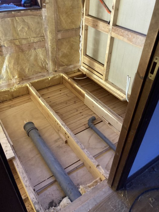 Rensat bjälklag i badrum med synliga rör och isolering, plywoodvägg och huntonittak.