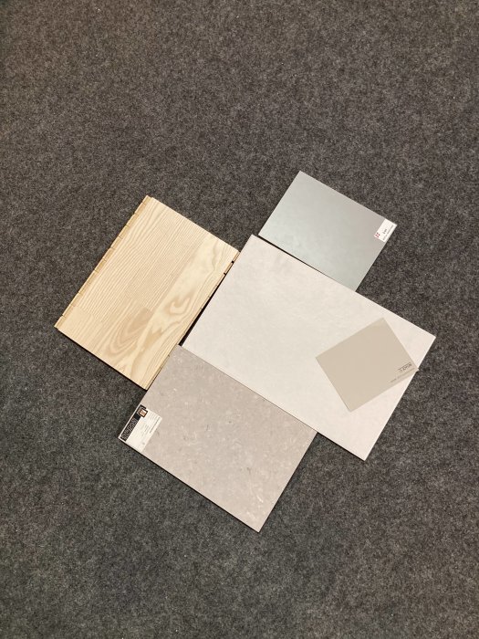 Fyra olika provkakel och plattor på grå matta, varav ett i träliknande mönster.